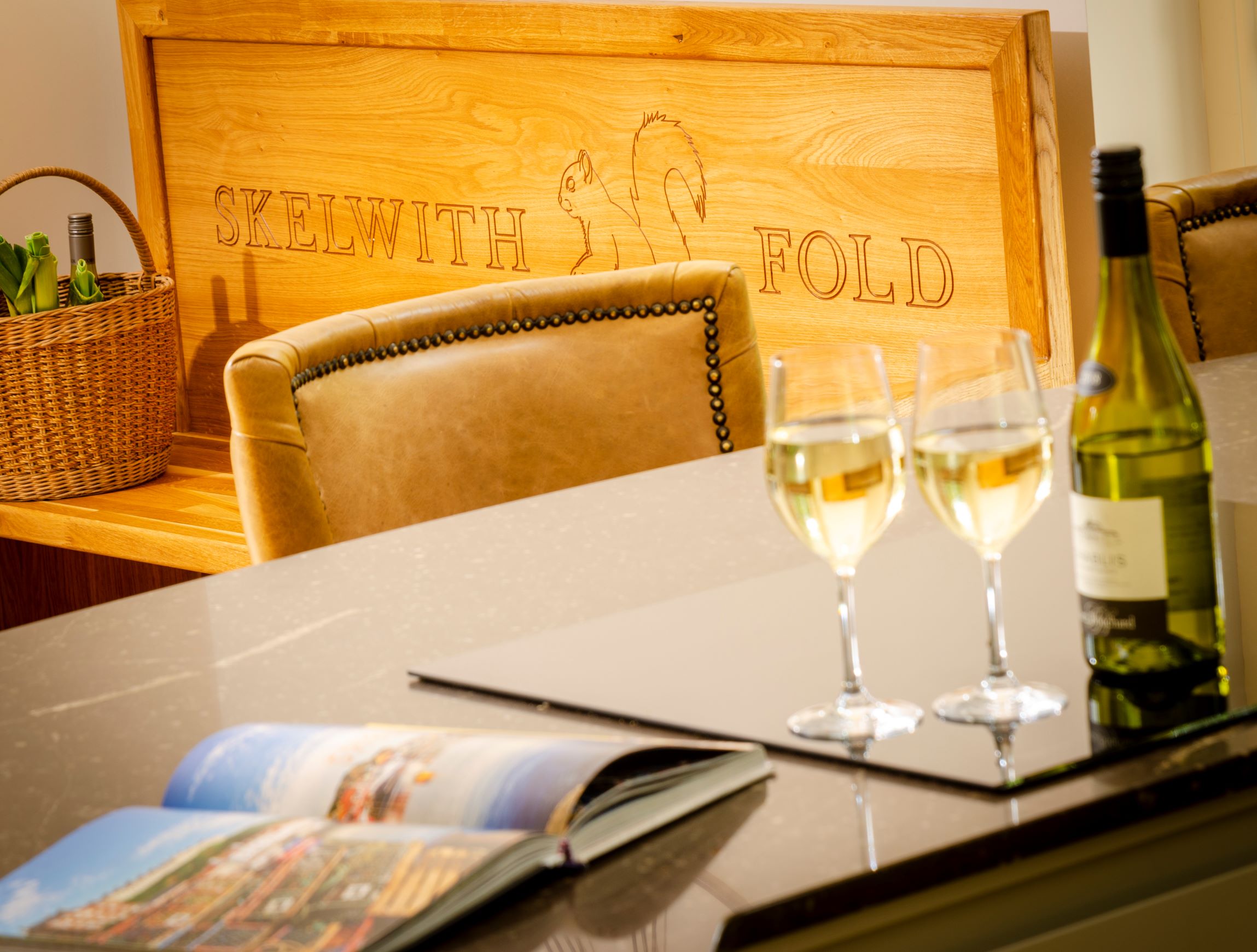 Skelwith Fold Cottages Greenhouse Kitchen Detail with wine on a marble counter and a Skelwith Fold branded wood bench in the background